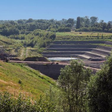 Een groen landschap onder een blauwe lucht. Op een van de hellingen is een trapsgewijze afgraving van een kleiput zichtbaar.