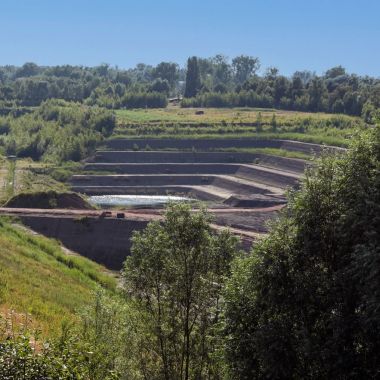 Een groen landschap onder een blauwe lucht. Op een van de hellingen is een trapsgewijze afgraving van een kleiput zichtbaar.