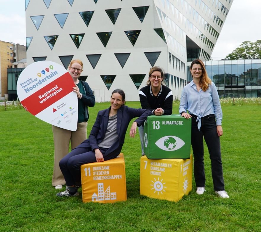 Vier personen poseren op het grasveld voor het Antwerpse Provinciegebouw. De persoon links draagt een bord met 'Energielandschap Noordertuin - Regionaal warmteplan'. De andere drie personen leunen op grote kubussen met verschillende opschriften: 'Duurzame steden en gemeenten', 'Klimaatactie' en 'Betaalbare en duurzame energie'. Dit zijn enkele van de SDG-doelstellingen, waar de provincie Antwerpen zich achter schaart. 