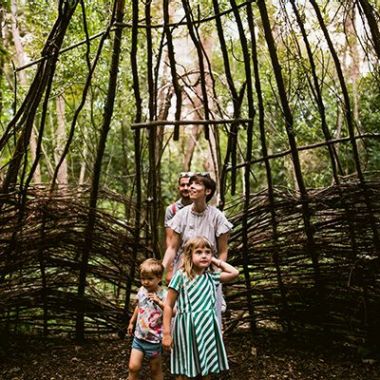 Een gezin met twee jonge kinderen gaat een wilgenhut in het Trollenbos van De Schorre in Boom binnen. Het wilgenriet is niet aansluitend, waardoor er licht binnenkomt, voornamelijk langs de bovenkant. De vrouw kijkt naar de dakconstructie boven haar dat licht doorlaat. Ze moedigt de kinderen met een klein duwtje in de rug aan om verder te wandelen, terwijl haar man achter haar volgt. De kinderen kijken vol bewondering rondom zich.