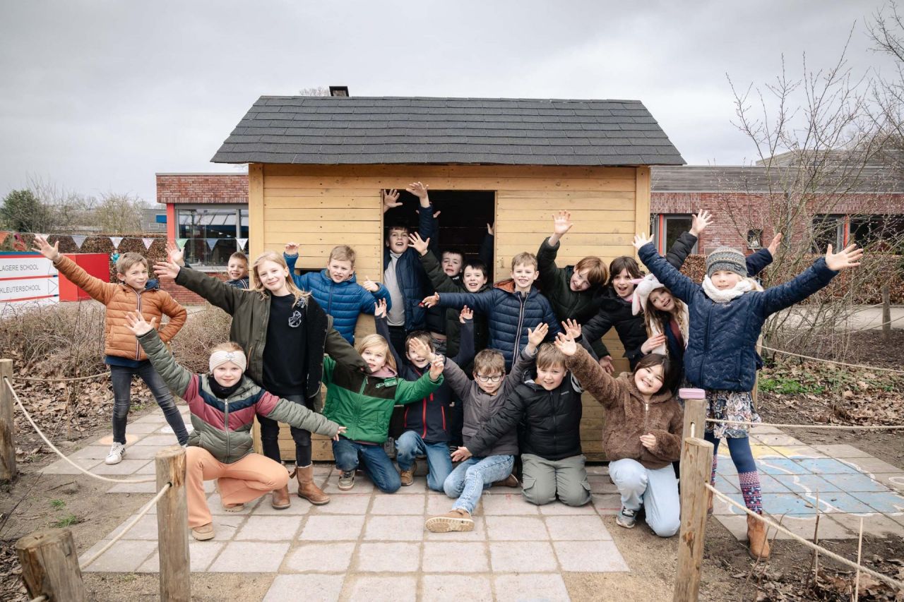 Leerlingen poseren blij voor het houten huisje op hun Groene Oase speelplaats.